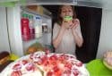 Woman in front of fridge eating sweets.