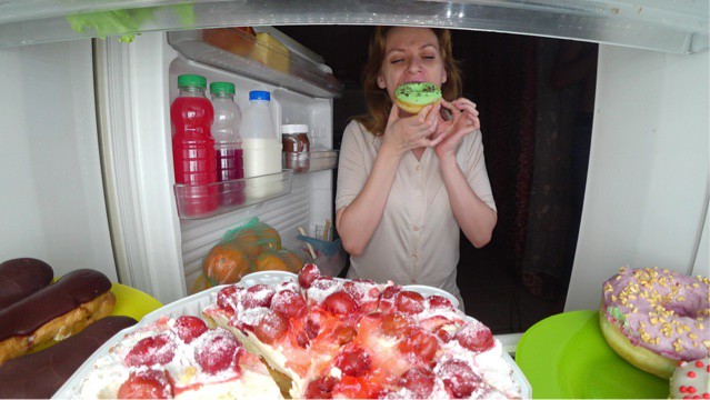 Woman in front of fridge eating sweets.