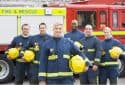 A group of firefighters standing in front of a fire engine.