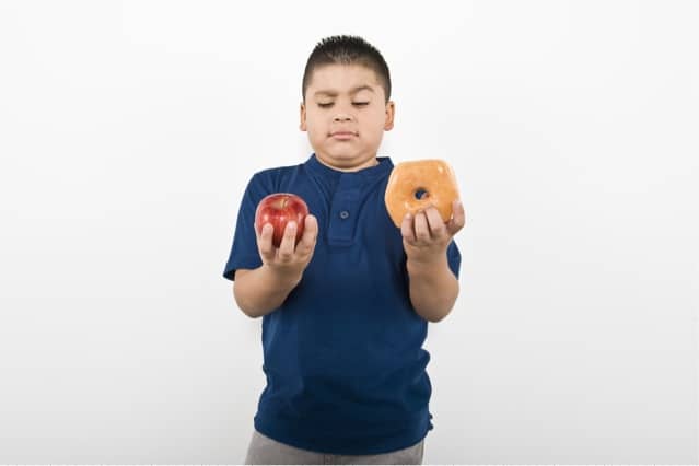 Boy choosing between apple and donut.