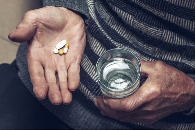 An elderly man takes pills with a glass of water.