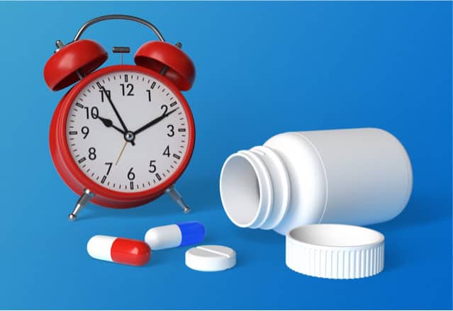 Alarm clock, tablets and white pills bottle on blue background.