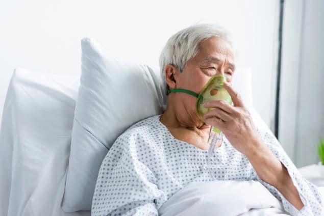 Senior asian patient on hospital bed with oxygen mask.