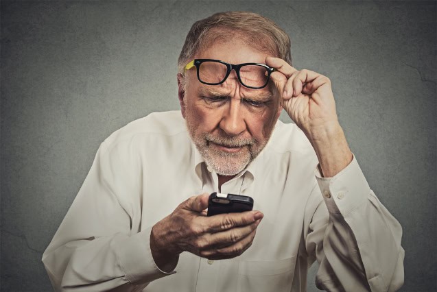 Elderly man with glasses having trouble seeing cell phone.
