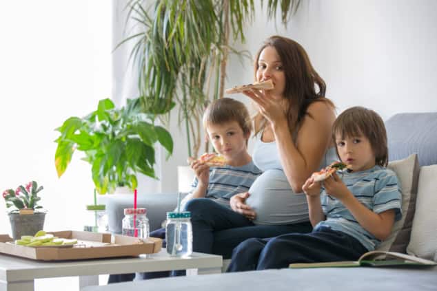Pregnant mother and two boys eating pizza.