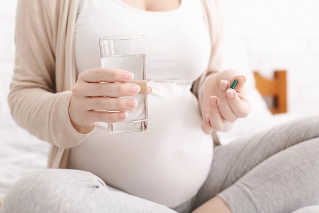Pregnant worman hoilding a pill and a glass of water.