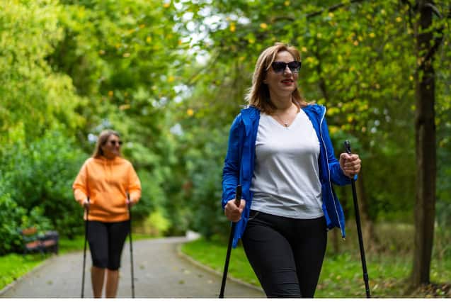 Two women practicing nordic walking in city park.