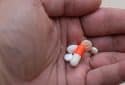 A close up photo of a hand holding five pills of different shapes and colors.